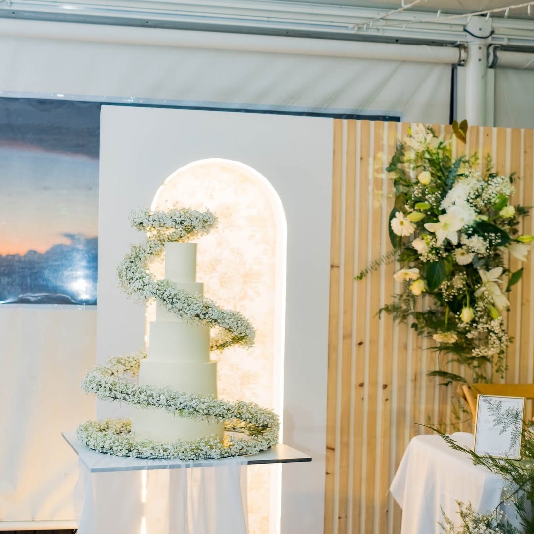 Gâteau de mariage enlacé de gypsophile devant une arche lumineuse